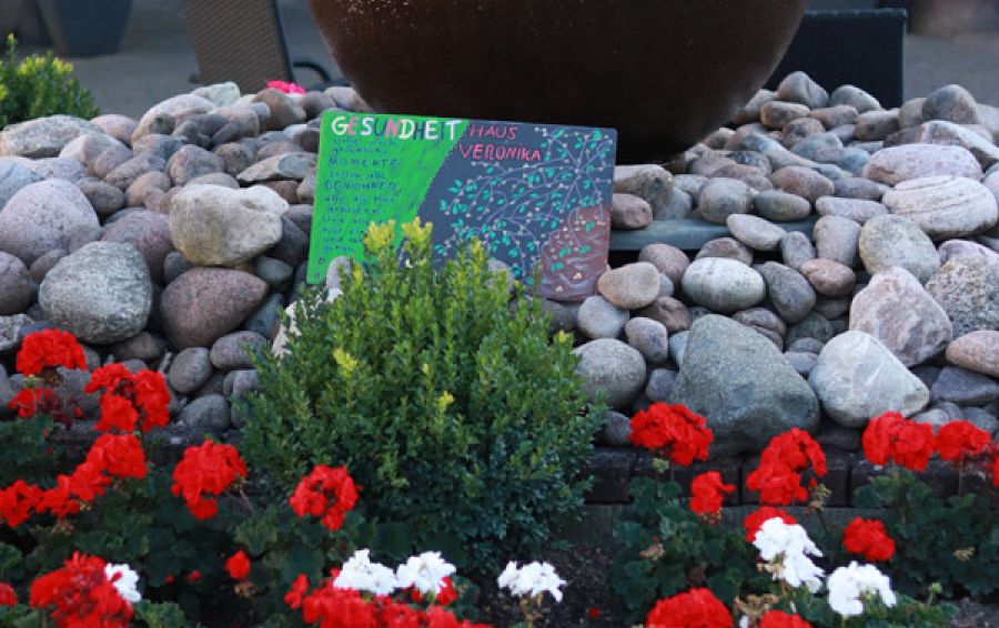 Eingangsbereich mit Willkommensgruss in Blumen und Steinen auf einer Schieferplatte